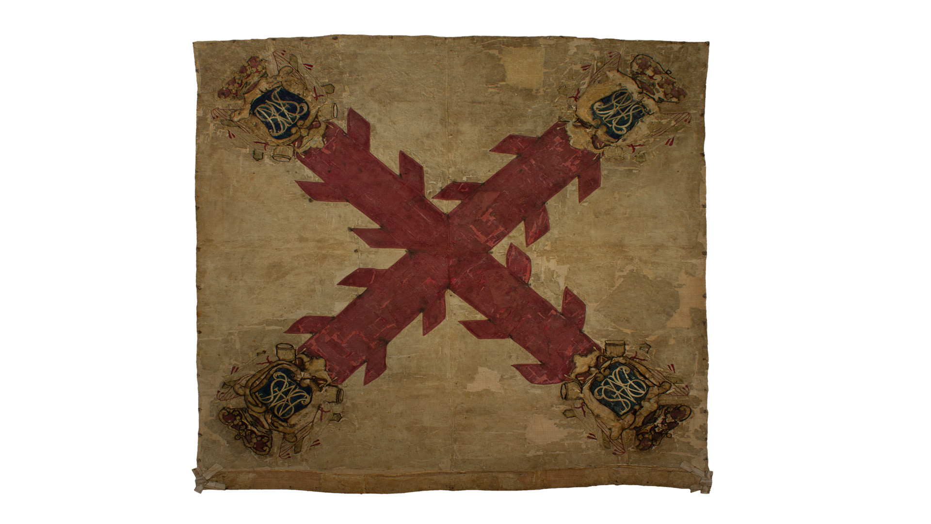 Bandera del Batallón Fernando VII en tafetán de seda y bordados. En el centro se observa una cruz roja con aspas en los brazos de la misma. Cada vértice rematado con un escudo con letras bordadas.